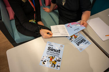 Pöydällä on Ohjaamon 10-vuotisjuhlaviikon esite, jota kaksi kättä pitelee.