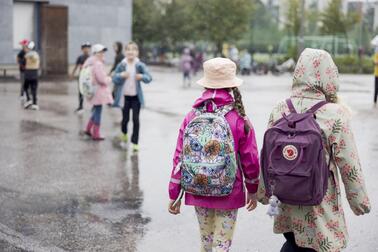 Kaksi lasta kävelemässä koulun pihalla sateisena päivänä.
