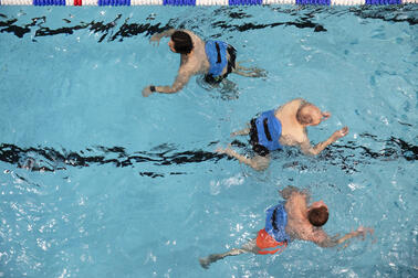 Kolme henkilöä uimassa altaassa yläpuolelta kuvattuna.