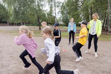 Lapset juoksemassa ulkona ohjaajan kanssa.
