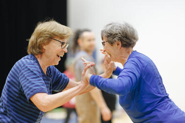 Kaksi iäkkäämpää henkilöä hymyilee ja pitää toisiaan kädestä kiinni. 