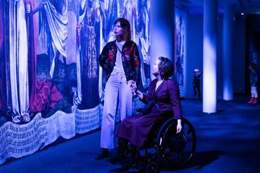 Kaksi henkilöä katselee seinälle ripustettua taidetta sinisävyisessä tilassa.