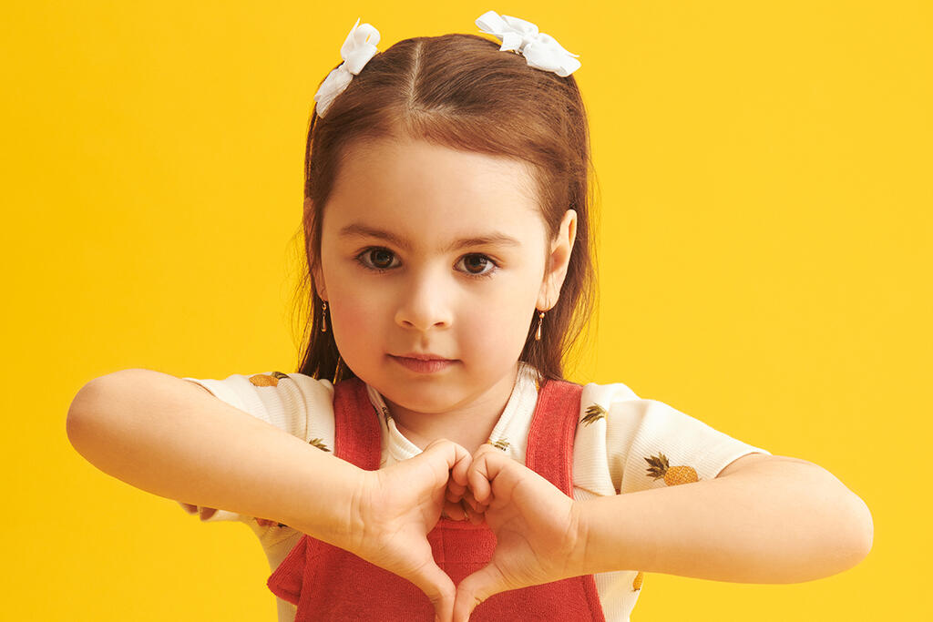 Lapsi tekee käsillään sydänkuvion keltaisen taustan edessä.