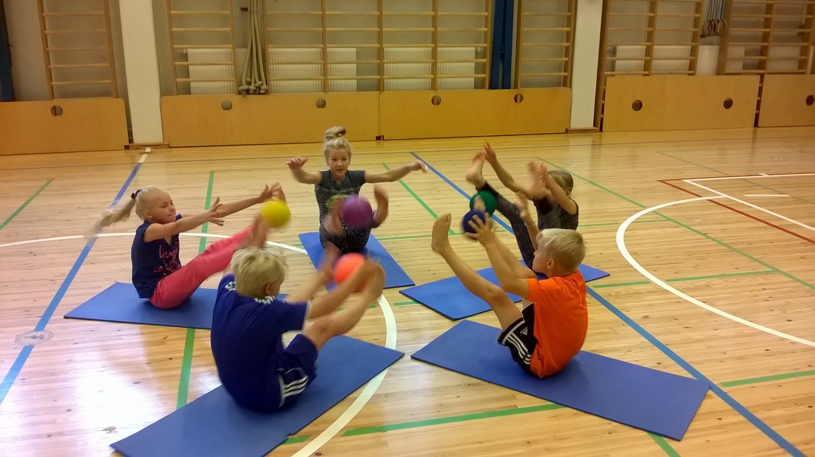 Lapsia jumppasalissa heittämässä palloja ilmaan