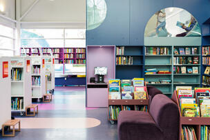 Blåtonade bokhyllor och en läsloft i Lillhoplax barnbiblioteks biblioteksal.